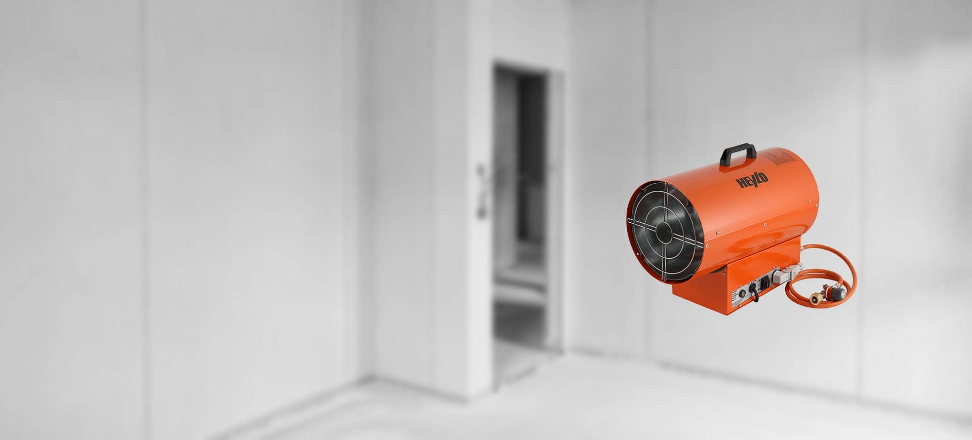 Oranger Gasheizer DG30 von Heylo mit Schlauch und Regler vor grauem Hintergrund in leerem Raum – professionelles Heizgerät für Bau- und Trocknungseinsätze.